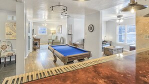A pool table in a room with a piano keyboard design on the floor, a chandelier, and a ceiling fan. - The Keys (Colorado Springs)
