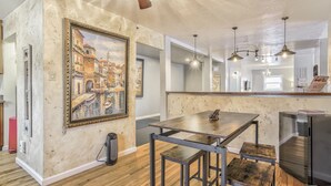 A kitchen with a wooden table, bar stools, a refrigerator, and a painting on the wall. - The Keys (Colorado Springs)