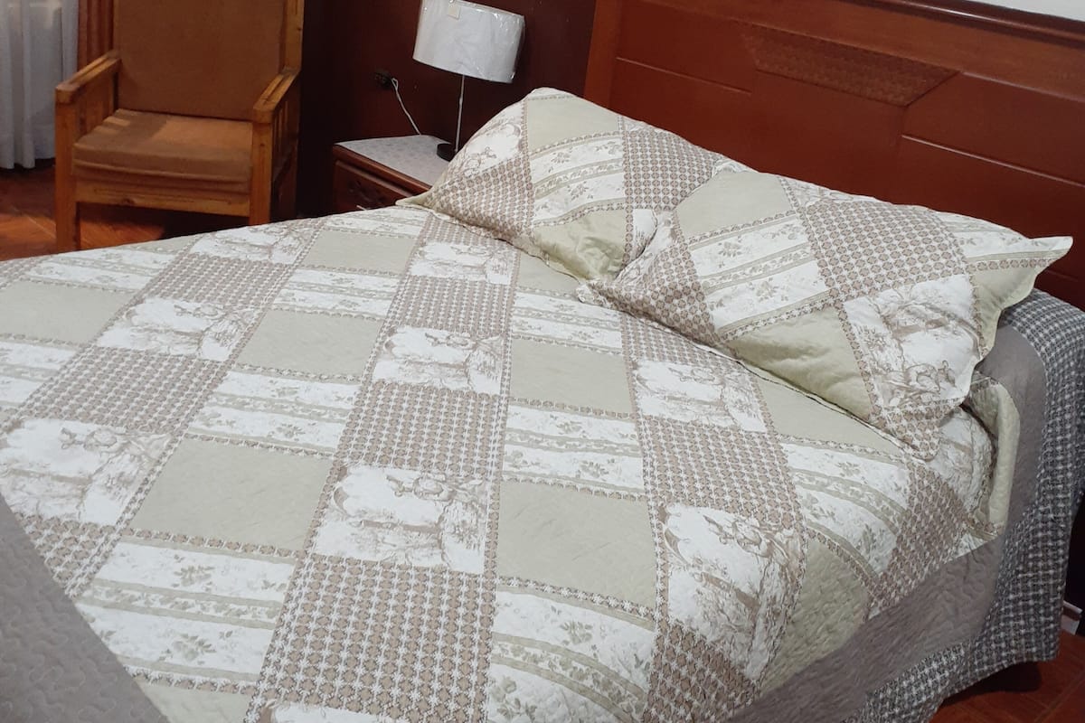 A hotel room with a bed, a chair, a nightstand, a lamp, and a painting on the wall.