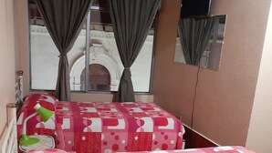 A hotel room with two beds, a window with curtains, a small table with a lamp, and a mirror on the wall. - HOTEL CENTRAL (Latacunga)