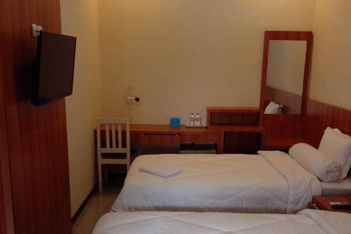 Hotellihuone, jossa on kaksi sänkyä, televisio, työpöytä ja peili.