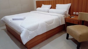 Una cama bien hecha con sábanas blancas, cabecera de madera, mesita de noche con lámpara y una silla.