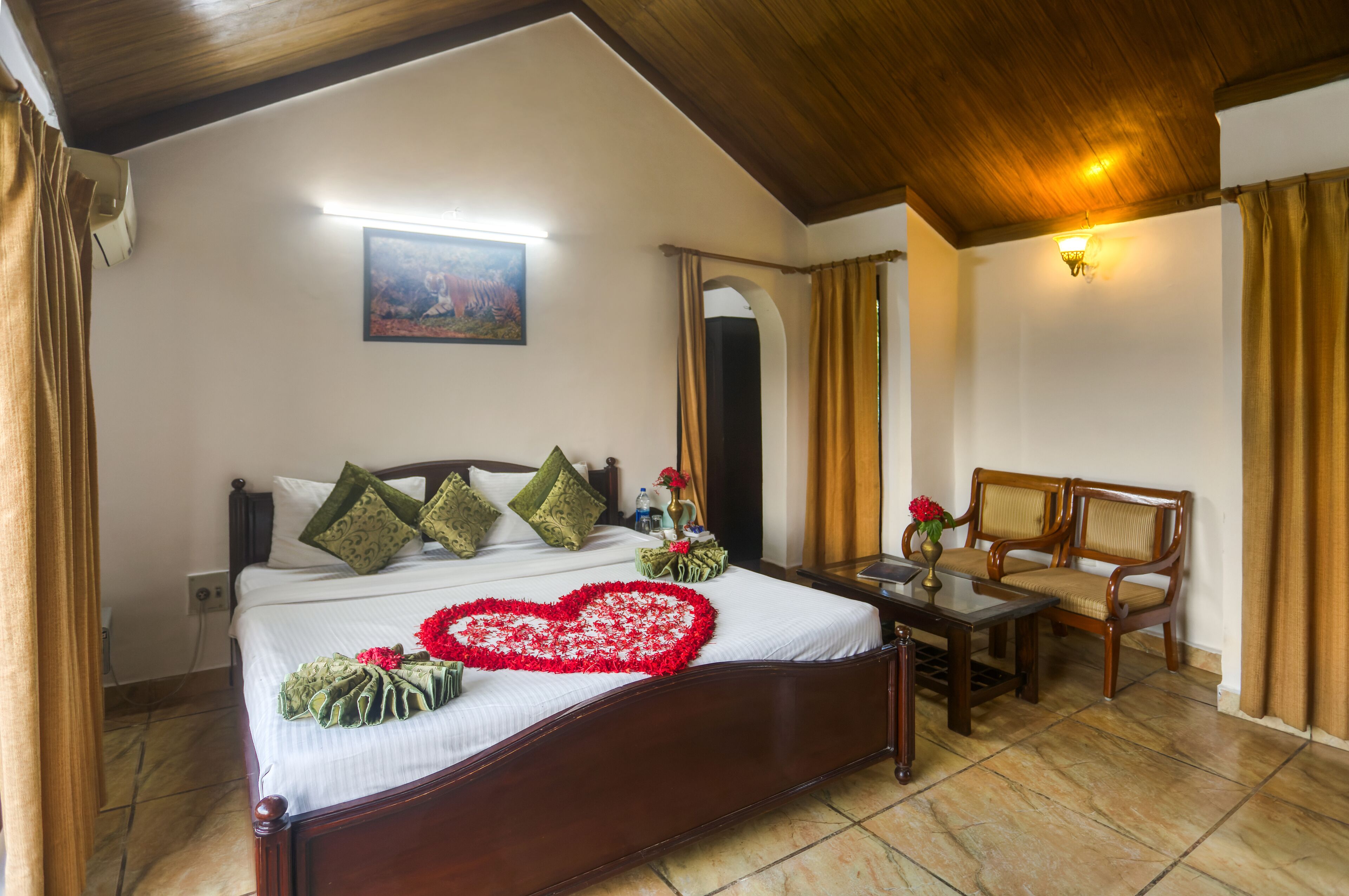 A neatly made bed with a heart-shaped decoration, a wooden headboard, and a bedside table with a vase of flowers.