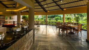 A covered dining area with a buffet setup, outdoor seating, and a view of a landscaped garden. - Tusk And Roar Resort Petfrindly Jungle Cottages (Ramnagar)
