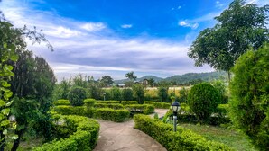 A garden pathway leading to a building with neatly trimmed hedges and a clear sky. - Tusk And Roar Resort Petfrindly Jungle Cottages (Ramnagar)