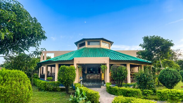 A building with a green roof, surrounded by well-maintained hedges and a stone pathway leading to the entrance. - Tusk And Roar Resort Petfrindly Jungle Cottages (Ramnagar)