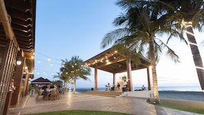 An outdoor seating area with palm trees and string lights, overlooking the ocean. - Asaricha Tropical Beach Resort (Pasuquin)