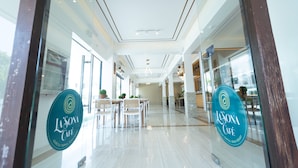 A modern interior with a glass door, a dining area with tables and chairs, and a sign for La Sona Café. - Asaricha Tropical Beach Resort (Pasuquin)