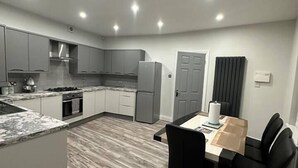 A modern kitchen with grey cabinets, a built-in oven, and a dining area with a table and chairs. - Immaculate 4-Bed detached House in Bootle (Bootle)