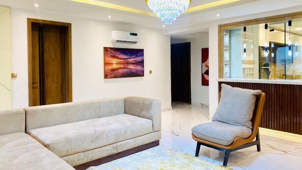 Un salon moderne avec un grand canapé, un fauteuil, un lustre et un tableau accroché au mur.