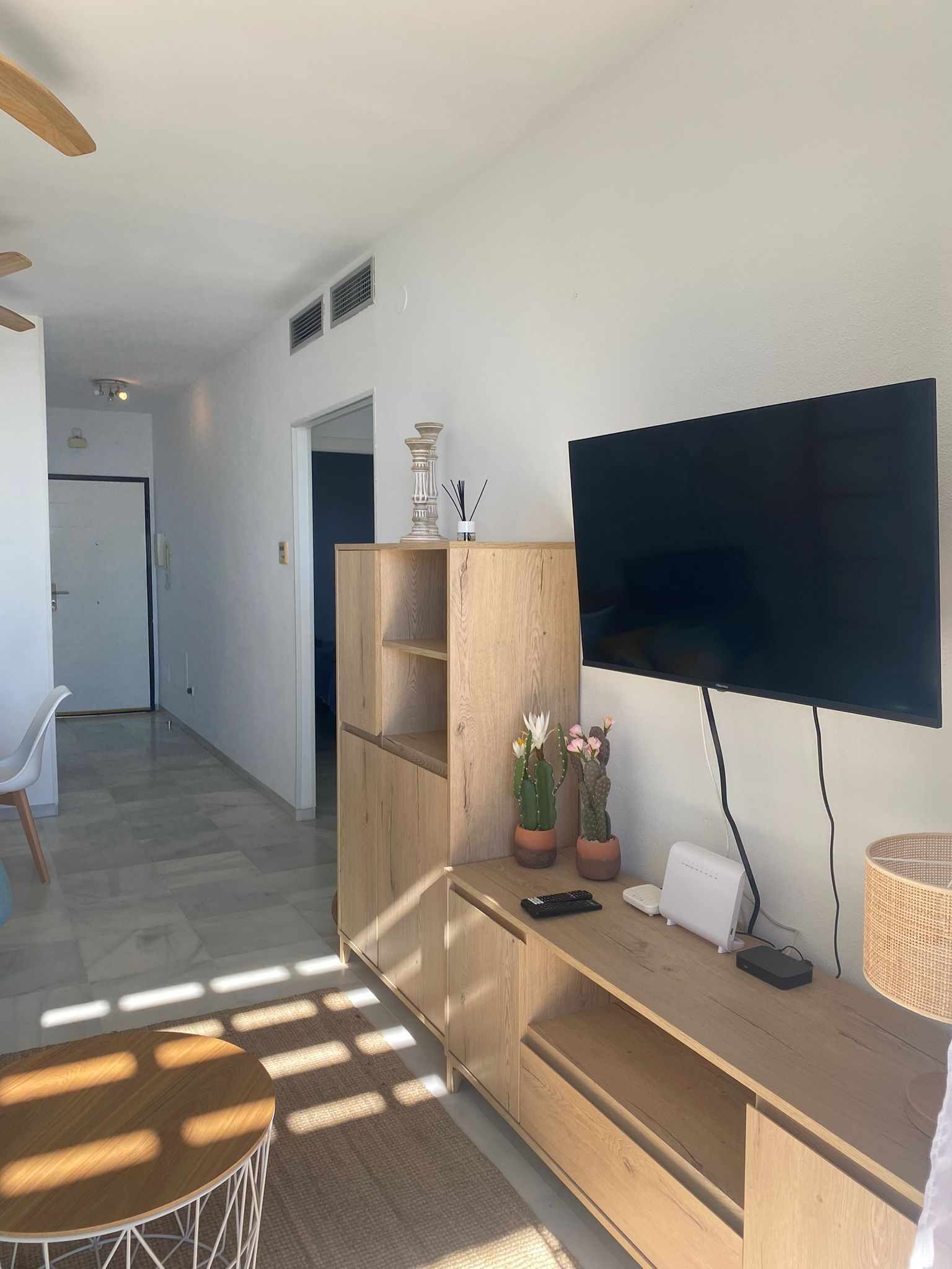 Un salon moderne avec un téléviseur à écran plat fixé au mur, un meuble de rangement en bois et une petite table sur laquelle repose une télécommande.