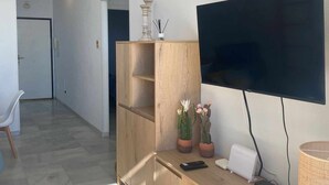 A modern living room with a flat-screen TV mounted on the wall, a wooden entertainment unit, and a small table with a remote control. - Beautiful apartment ideal for families (Mojacar)