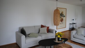 Una sala de estar con sofá, una mesa de centro, una lámpara colgante y una obra de arte enmarcada en la pared.