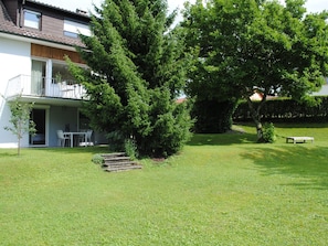 A residential property with a well-maintained lawn, a large coniferous tree, a patio with outdoor furniture, and a building with a balcony.
