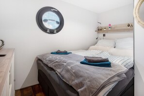 A bedroom with a bed, a round mirror, a wooden shelf with decorative items, and a window with a view.