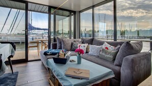 A modern living area with a sofa, coffee table, and a view of boats through large windows.