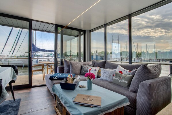 A modern living area with a sofa, coffee table, and a view of boats through large windows.