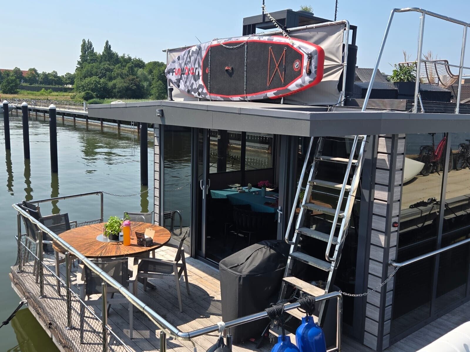 A floating house with a deck, outdoor seating, and a covered area.