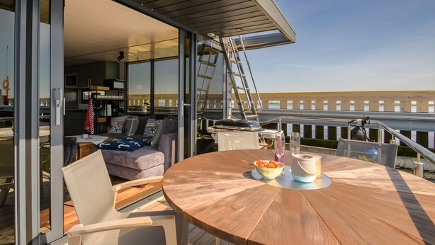 A wooden deck with a round table, a grill, and a ladder.