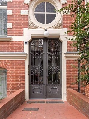 Ein Gebäudeeingang mit einer Doppeltür und einem runden Fenster darüber, Fassade aus Ziegelsteinen.