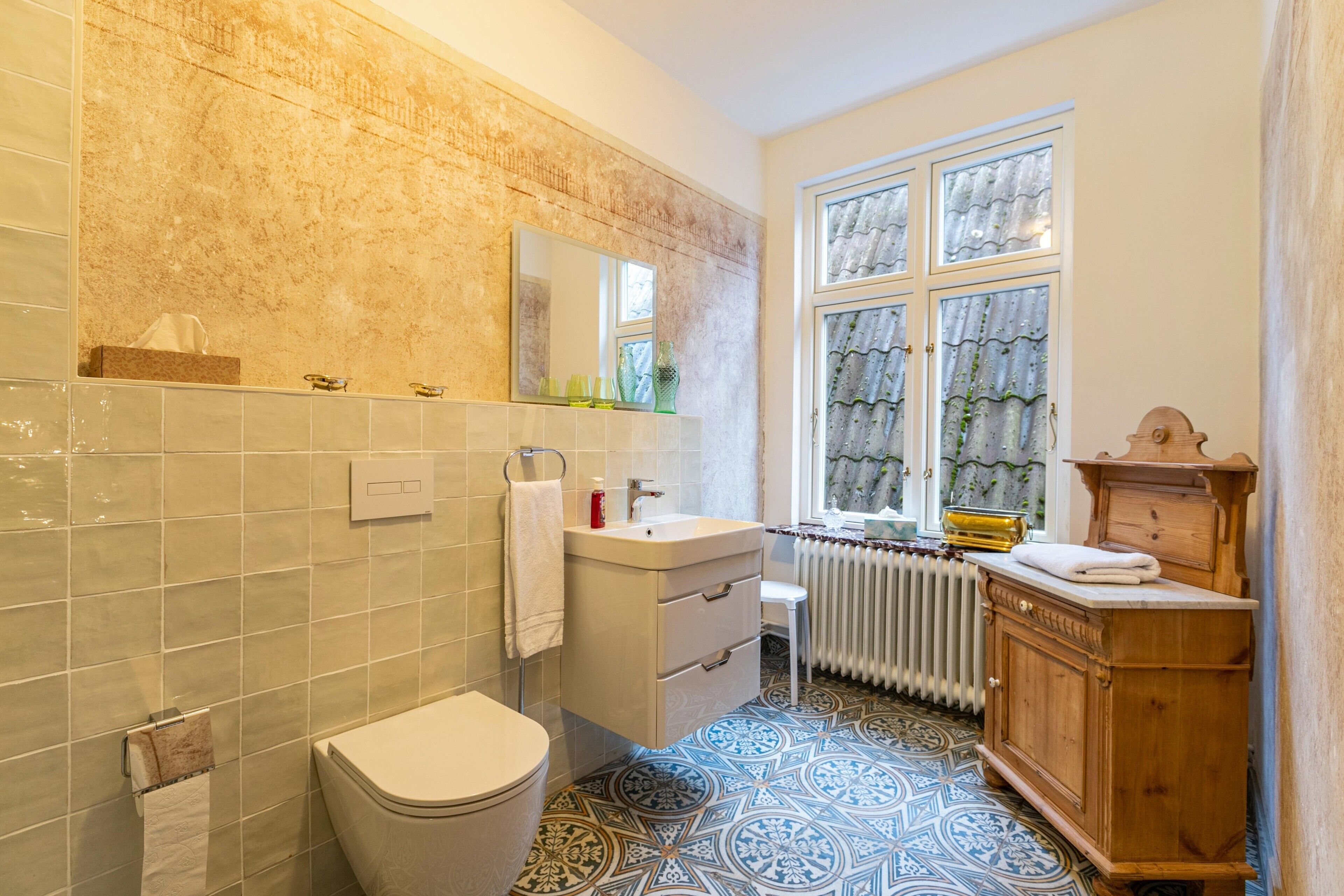 A bathroom with a toilet, sink, mirror, and window with curtains.