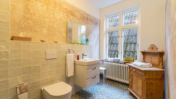 A bathroom with a toilet, sink, mirror, and window with curtains.