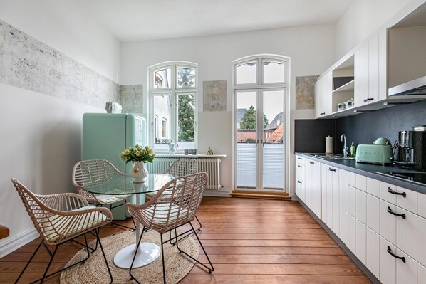 Une cuisine moderne avec un coin repas, des meubles blancs et une vue dégagée sur l’extérieur grâce à une grande fenêtre.