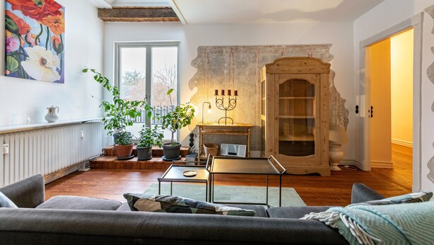A living room with a fireplace, wooden beams, a large window, and a sofa. - Apartment 'Wohnoase Im Denkmal' with Private Terrace, Balcony and Wi-Fi (Garding Kirchspiel)