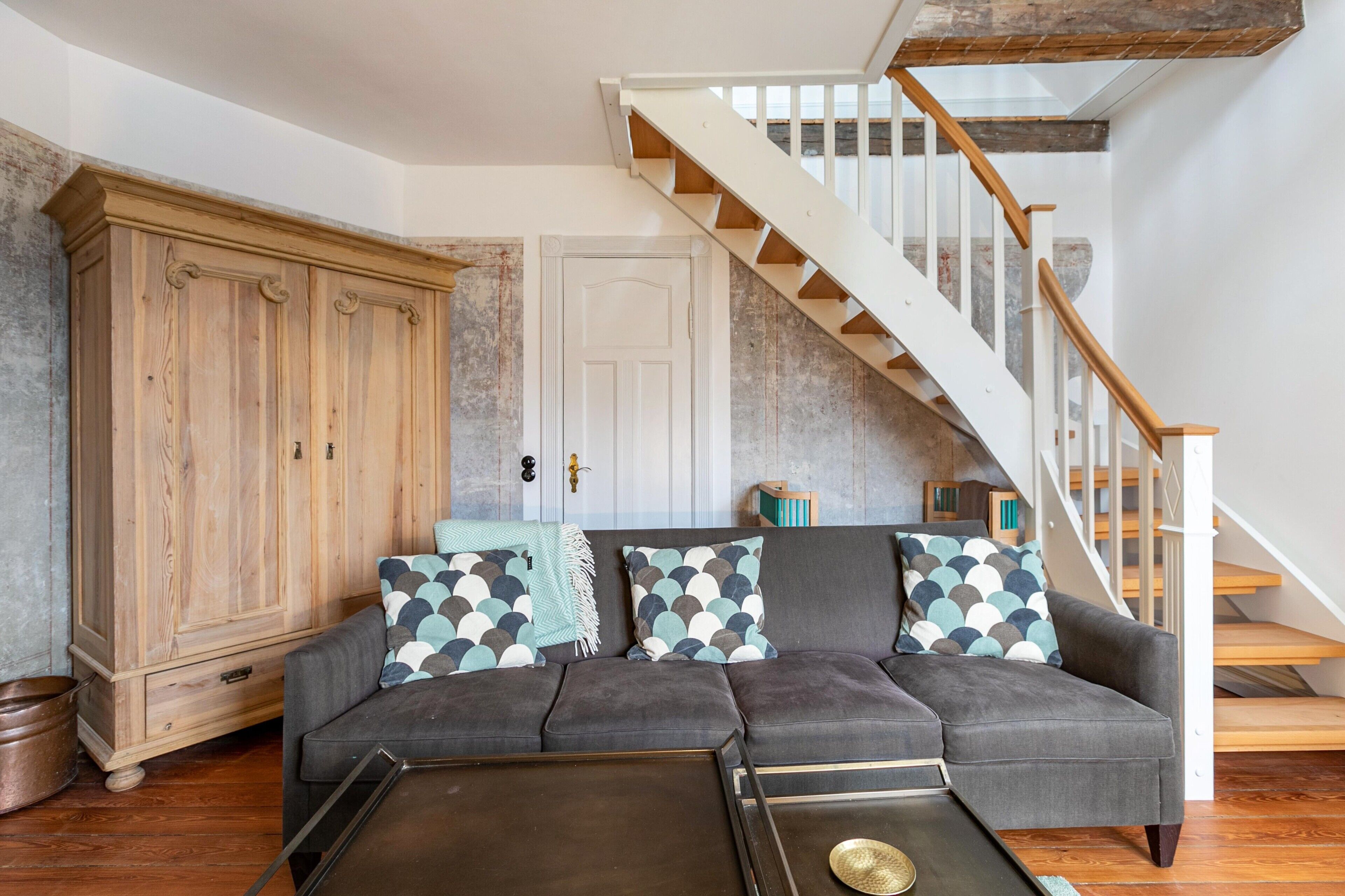A living room with a gray sectional sofa, a wooden cabinet, a coffee table, and a staircase with wooden steps.