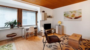 A modern living room with a wooden ceiling, a TV, a desk, a chair, a sofa, and a potted plant. - Apartment "Eva Maria" with Balcony and Wi-Fi (Pforzheim)