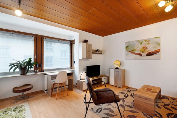 Un salon moderne avec un plafond en bois, une télévision, un bureau, une chaise, un canapé et une plante en pot.