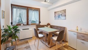 A compact living space with a dining table, chairs, a bench, a radiator, a potted plant, a small cabinet, and a window with curtains. - Apartment "Eva Maria" with Balcony and Wi-Fi (Pforzheim)