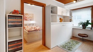A compact room with a bed, a small kitchenette, a stool, and a window with a plant. - Apartment "Eva Maria" with Balcony and Wi-Fi (Pforzheim)