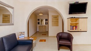A hotel lobby with a leather sofa, a brown armchair, a wooden table, a TV mounted on the wall, and a wooden bookshelf. - Villa & Pool 2 Mellieħa Bay Retreat, Mellieha, Malta (Mellieha)