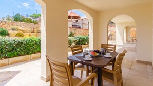 A dining area with a table set for two, surrounded by arches, with a view of a stone wall and greenery outside. - Villa & Pool 2 Mellieħa Bay Retreat, Mellieha, Malta (Mellieha)