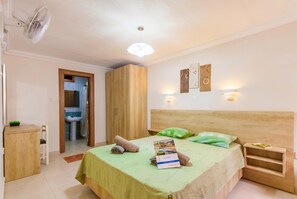 A bedroom with a bed, bedside tables, a desk, a wardrobe, a fan, a light fixture, and a wall-mounted artwork.