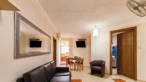 Un couloir avec un canapé en cuir noir, une table à manger avec des chaises, un téléviseur fixé au mur et une porte en bois.