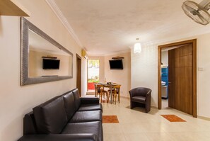 A hallway with a black leather sofa, a dining table with chairs, a TV mounted on the wall, and a wooden door.