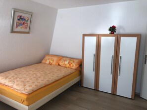 A bedroom with a bed, a wardrobe, a framed picture on the wall, and a small potted plant.