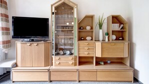Ein Wohnzimmer mit Fernseher, Holzakzepten, einer Vitrine und Regalen mit Dekoration.