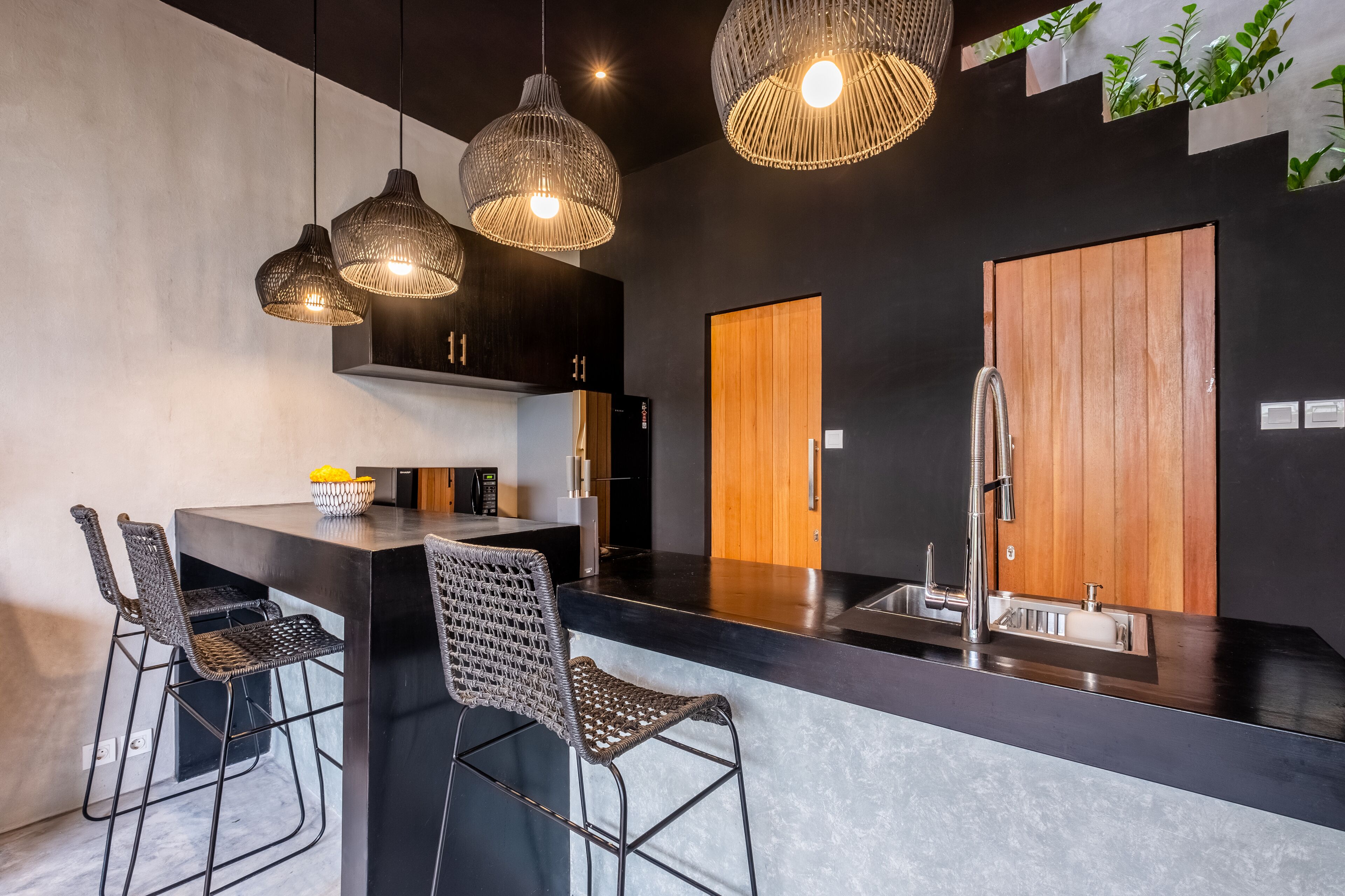 Eine moderne Küche mit schwarzem Arbeitsplatz, drei Korbtropflichten und einer Holztür.