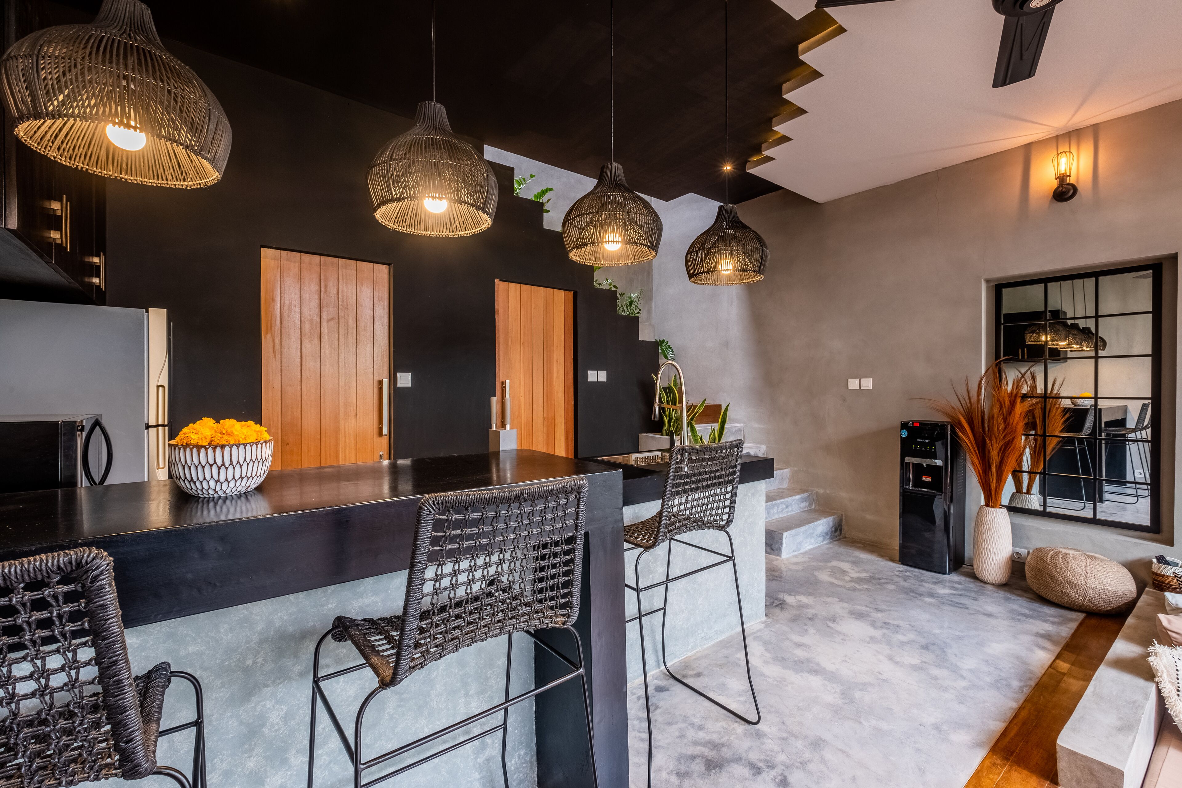 Una cucina moderna con un piano di lavoro nero, sgabelli da bar in vimini e luci a sospensione.