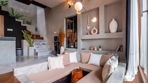 A modern living room with a sectional sofa, a staircase, and a large window. - Hebe Villa by Betterplace (Canggu)