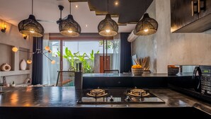 A modern kitchen with black countertops, a gas stove, and hanging pendant lights. - Hebe Villa by Betterplace (Canggu)