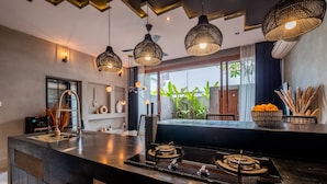 A modern kitchen with a central island, pendant lighting, and a view of the outdoors. - Hebe Villa by Betterplace (Canggu)