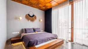A modern bedroom with a wooden ceiling, a bed with a wooden platform, and a large window with sheer curtains. - Hebe Villa by Betterplace (Canggu)