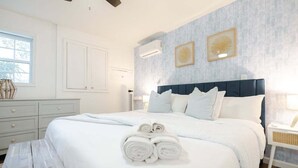 A neatly made bed with rolled towels, a dark blue headboard, and two framed artworks on the wall. - Coastal Cozy and Close to Beach with Turf Yard! (Carolina Beach)