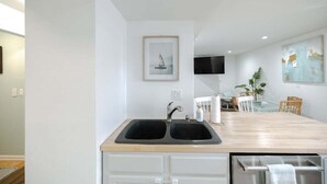 A modern kitchen with a double sink, wooden countertop, and a dining area with a table and chairs. - Coastal Cozy and Close to Beach with Turf Yard! (Carolina Beach)