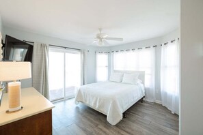 A bedroom with a bed, a ceiling fan, a TV on the wall, and a window with curtains. - Ocean Views + Across from Beach Access! (Surf City)