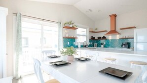 A modern kitchen with white cabinetry, teal backsplash, and wooden shelves. - Ocean Views + Across from Beach Access! (Surf City)